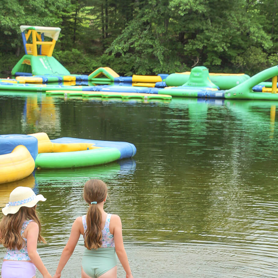Two girls walking into the lake with a blow up water toy in the water